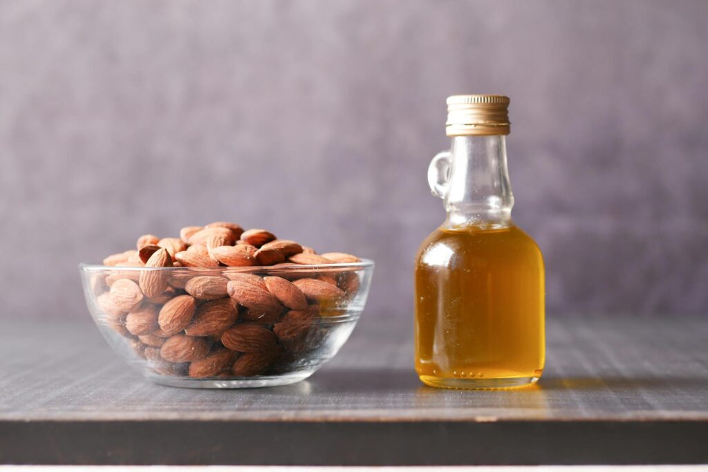 Mandel- & Borretschsamenöl-A close-up of almonds in a glass bowl alongside a bottle of almond oil.-photo-AETERNA-X