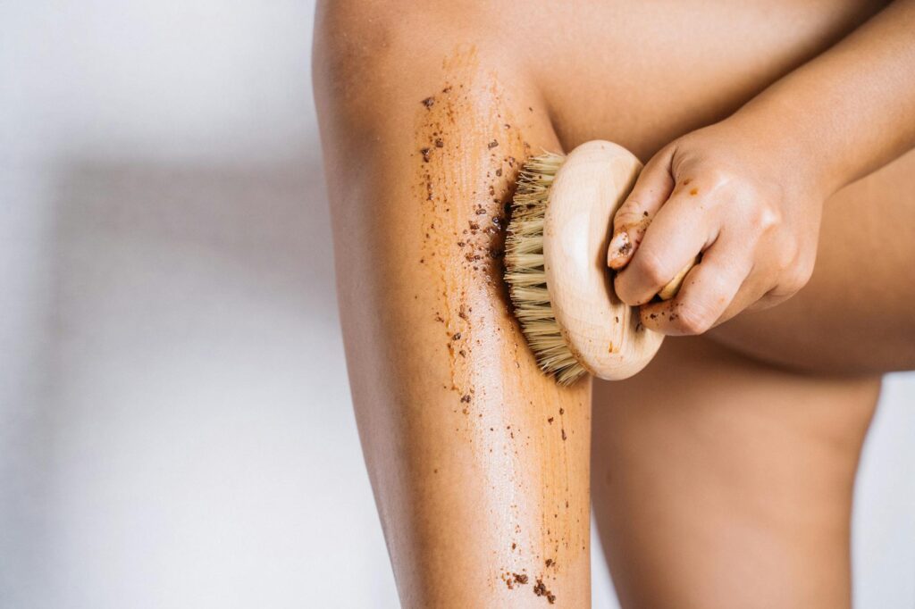 Warum Deine Hormone bestimmen, ob Du Cellulite bekommst-Detailed image of a hand using a brush for exfoliating a leg, showcasing skincare routine.-photo-AETERNA-X